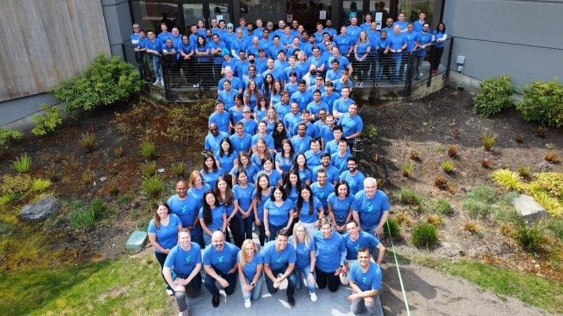 Truveta employees wear blue shirts and stand together to form the letter "T"