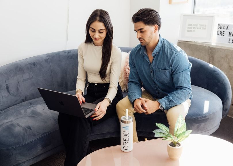 Two Crexi team members look at information on a laptop computer screen while working together in the company’s office