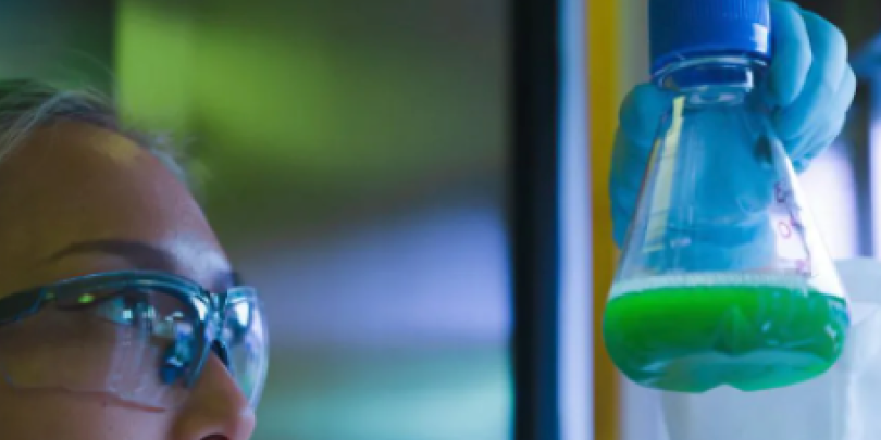 A lab tech mixing a green solution in a flask.