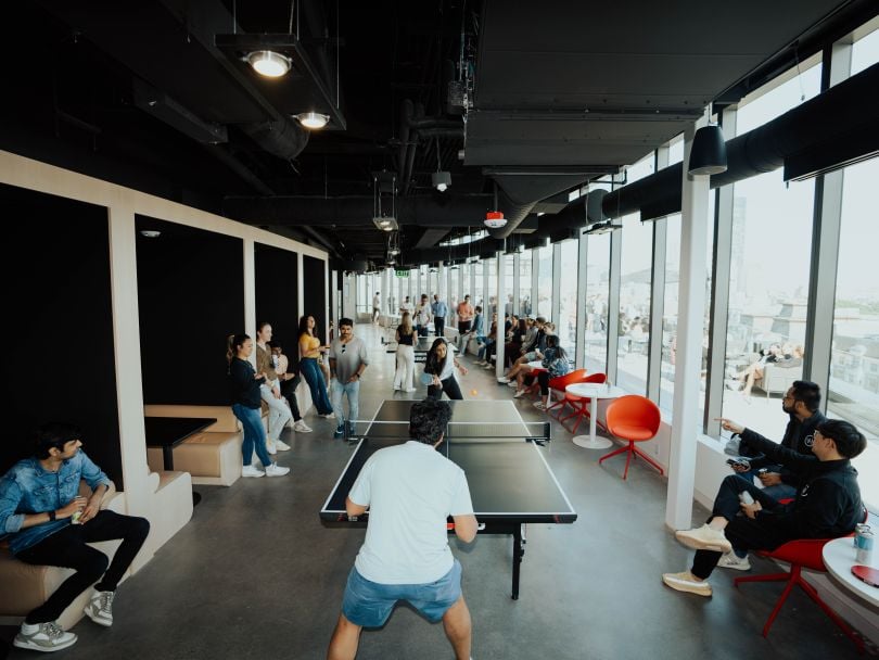 Two team members playing ping pong in office as others watch