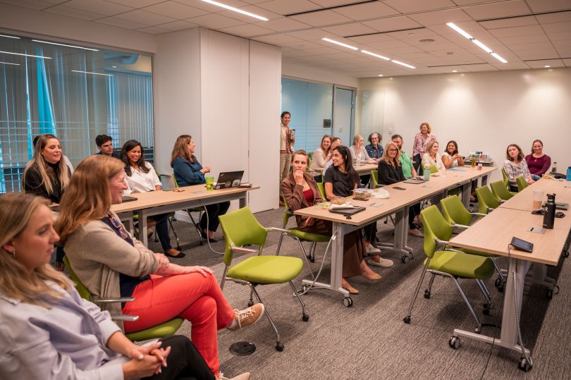 employees sitting in on a meeting with long tables and green chairs