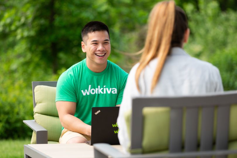 Employee with Workiva T-shirt sits outside facing colleague, smiling.