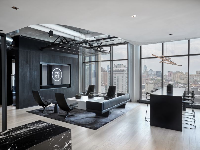 A photo of Yext’s New York office with black and white furniture and windows displaying a view of the city.