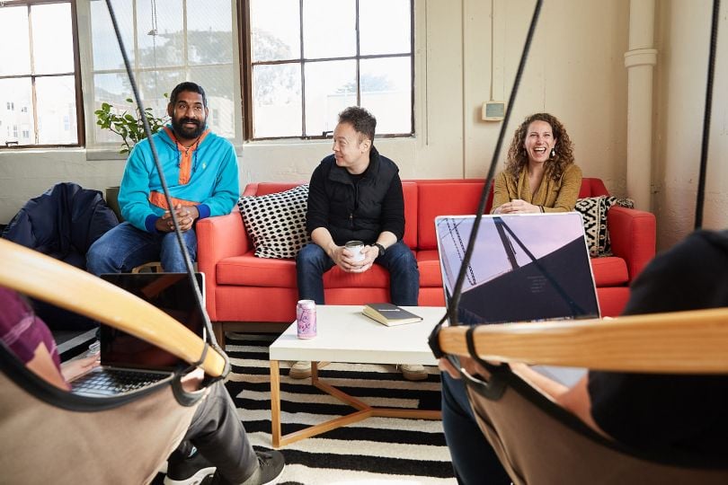 team meeting on red couch with five members and a small white square desk