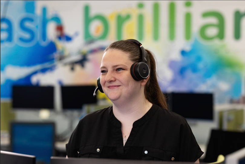 An Alliant team member wearing a headset smiles, looking at something off-screen.