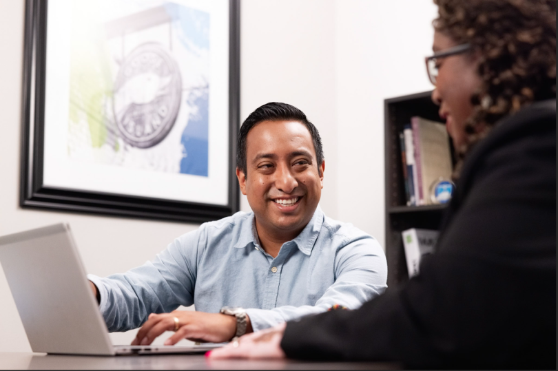 A man and woman sit together near a laptop, both smiling.