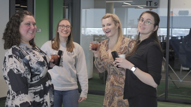 Four employees with drinks pause conversation to smile for camera