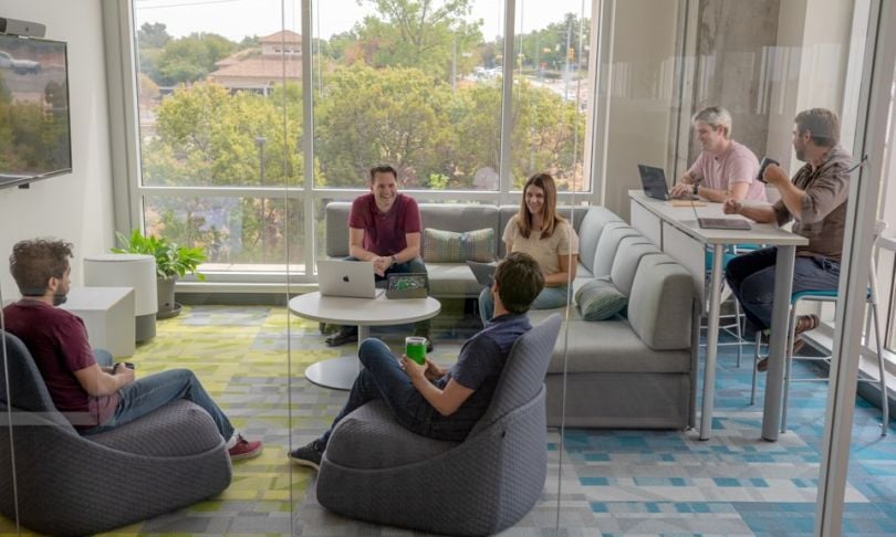 Six Brinqa team members work in a shared lounge area, talking and smiling.