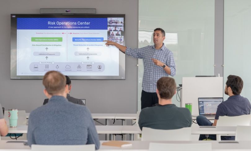 Alex Babar presents at a screen in front of a room of Brinqa coworkers.