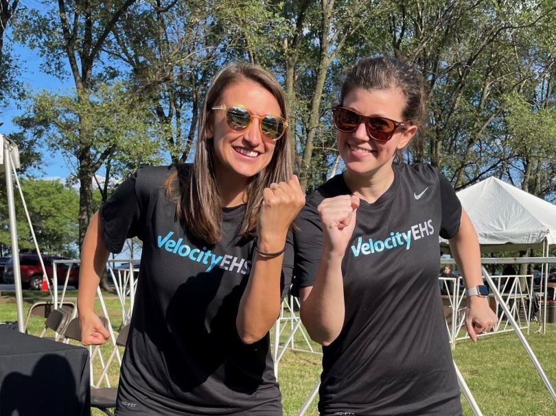 Two VelocityEHS team members in a runner’s pose in outdoor party setting.