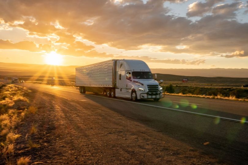 A truck drives through the prairie at sunset.