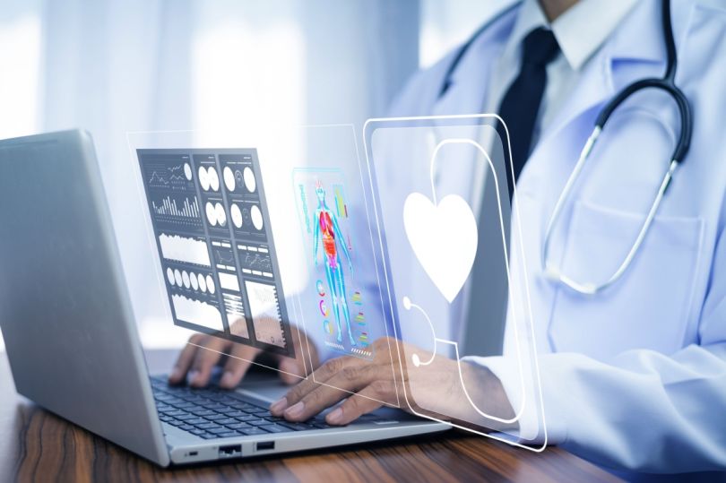 A doctor working on a laptop with holographic health charts.