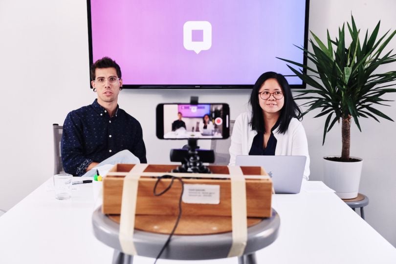 Two people look toward an iPhone on a tripod that is recording in the foreground