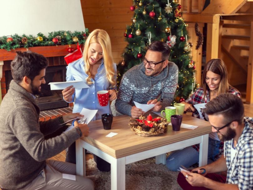 Team members gather around a small table while creating paper snowflakes during an office holiday party. 