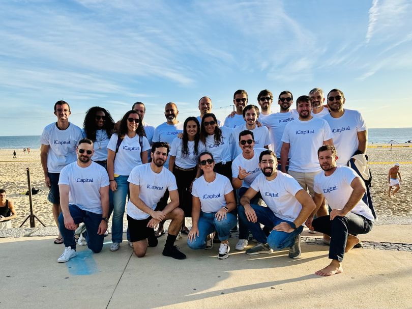 iCapital employees pose for a group picture in matching t-shirts on the beach.