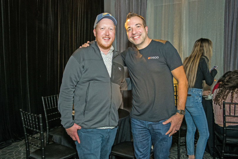 Tim Shea stands with a colleague at an indoor event. 