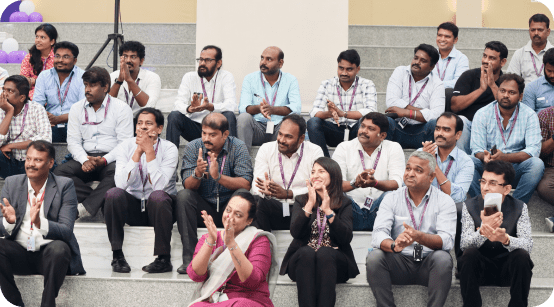 Candid photo of team members seated in stadium-style seating, smiling and clapping