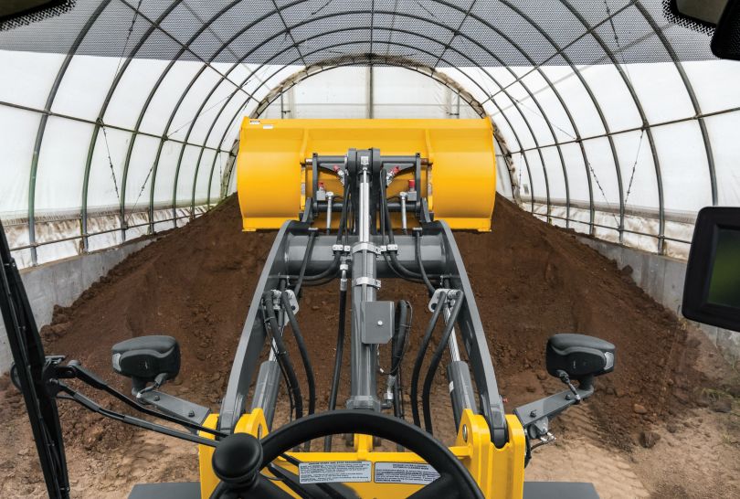 John Deere machinery moves dirt in a covered farm area. 