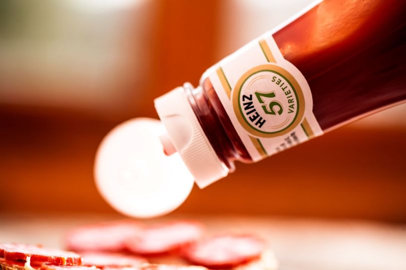 A bottle of ketchup being poured onto a dish.