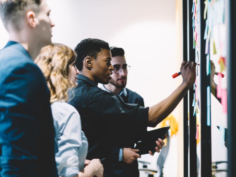 Man writes notes on sticky note during brainstorming session as colleagues watch