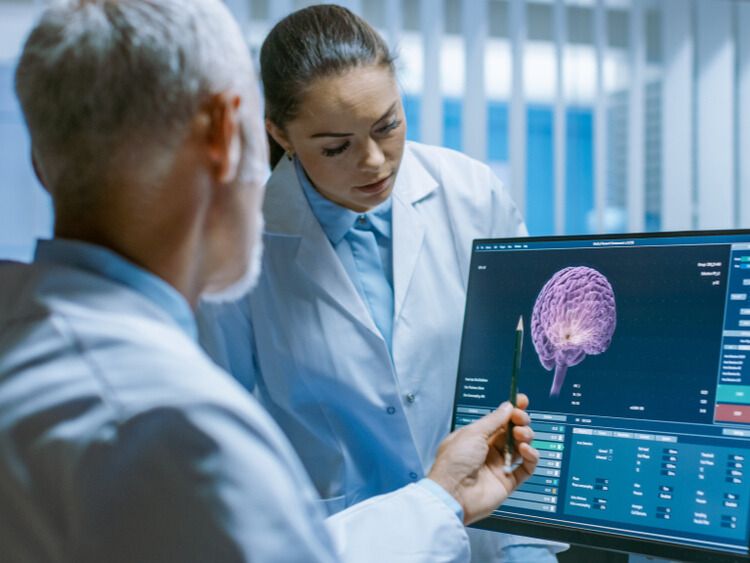 Cancer researchers looking at image of human brain on computer monitor