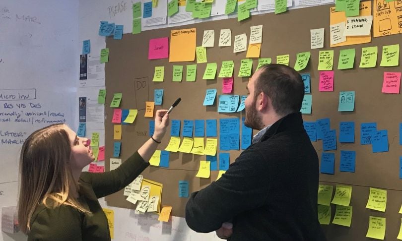 Two PNC team members participate in a design thinking exercise using colorful sticky notes on a wall.