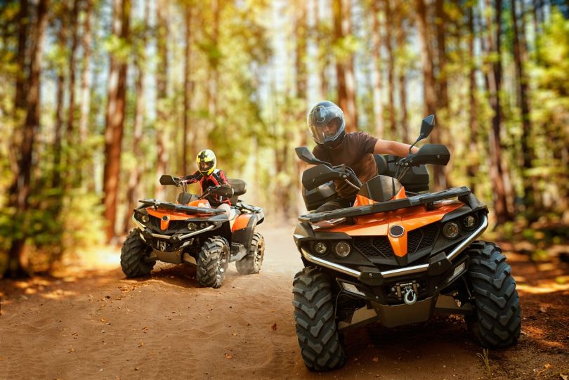 Two people riding quad bikes through a forest trail.