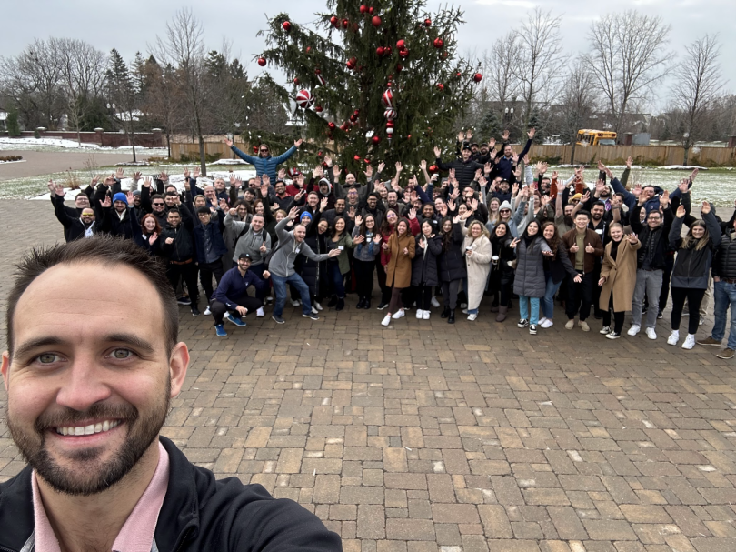 A group of Roofr team members pose with a large holiday tree in an outdoor plaza.