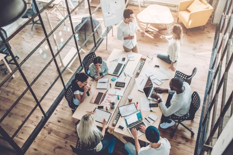 Coworkers in a meeting space with laptops, paper and pens having multiple discussions, photographed from above.