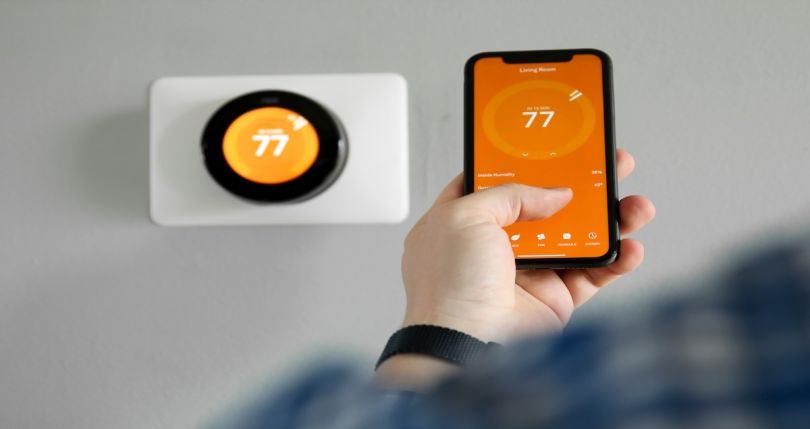 Person using phone to control smart thermostat. 