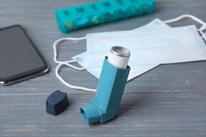 An image of an inhaler with medication and a smart phone in the background.