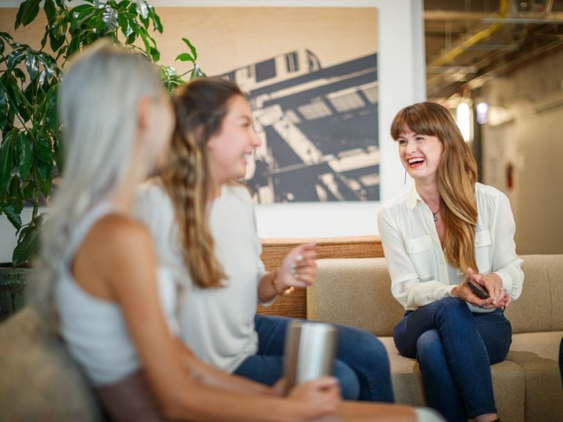 Three VelocityEHS team members sitting, talking and laughing in the office.