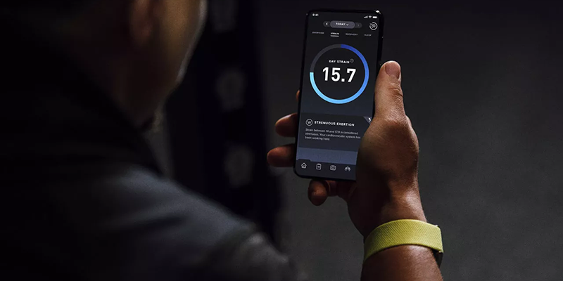 A person holding their smartphone and wearing Whoop’s fitness tracker on their wrist.