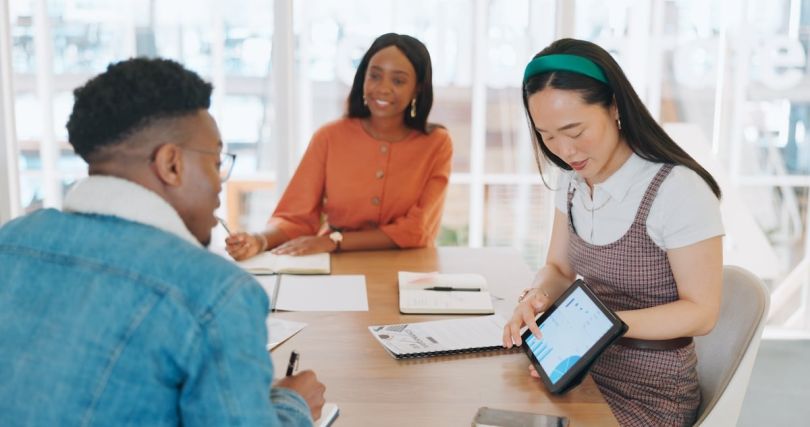 Three professionals engaged in a discussion around a table, with one of them using a tablet.