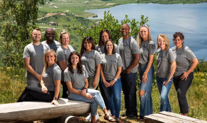 Tilt staff posing for a photo in front of a lake.