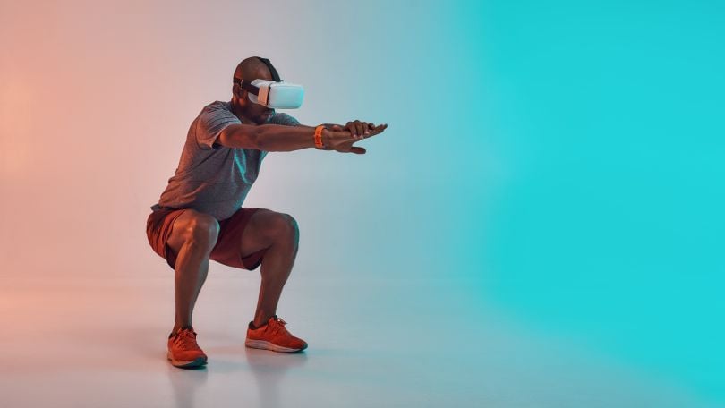 A man in a VR headset, squatting and holding his arms out in a workout pose.