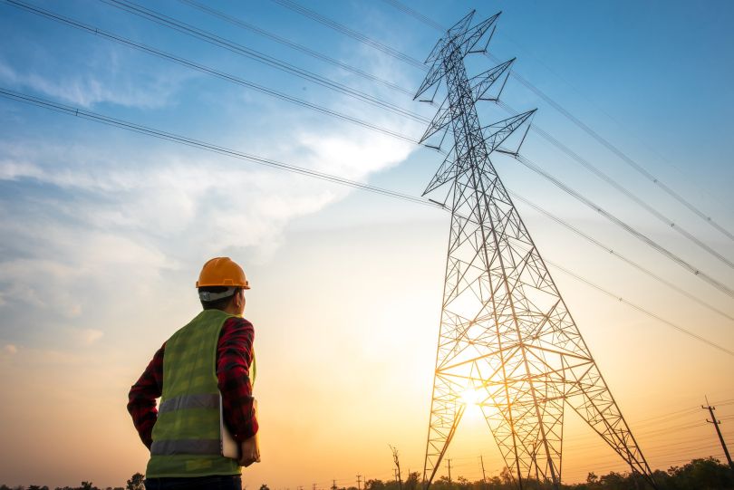 A worker stares up at an electricity tower.