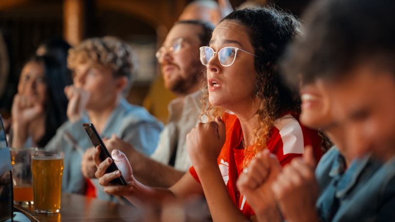 A woman holding a smartphone and watching sports at a bar
