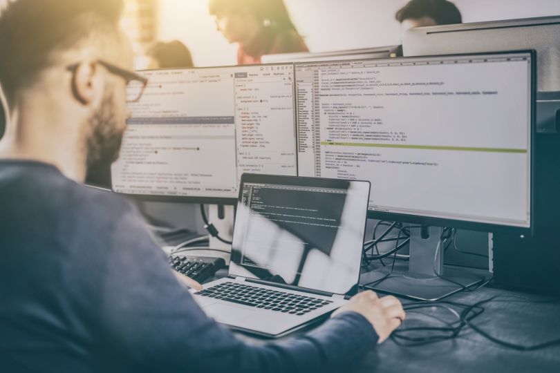 Developer writes code on a computer with multiple screens.