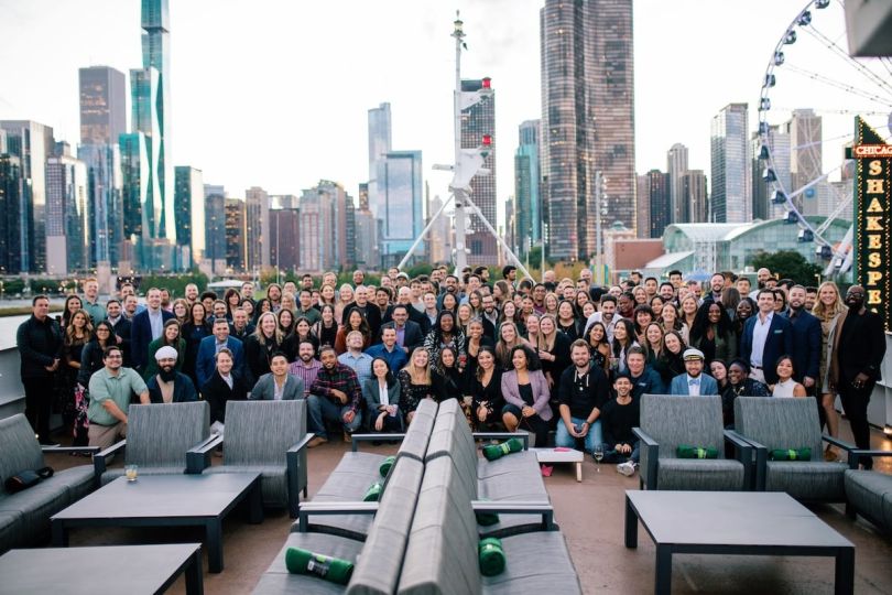 A large group of Vouch professionals pose for a group photo in front of the Chicago skyline.