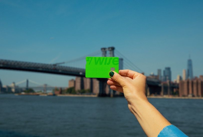 A hand holds a Wise card in front of a city skyline.