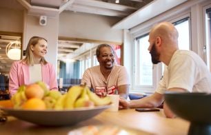 Three people chatting around a table in the office kitchen